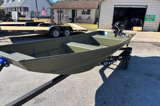 The Image of 2026 Lowe L1436L Jon boat on trailer, parked outdoors near a garage. - 2