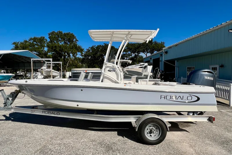 The Image of 2024 Robalo 206 Cayman boat on trailer, parked outdoors near blue building. - 1