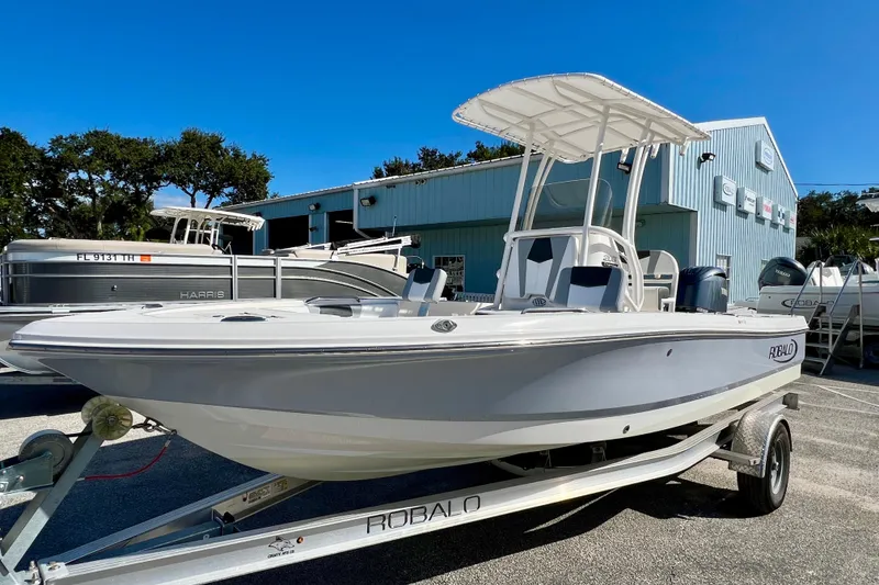 Slide: The Image of 2024 Robalo 206 Cayman boat on trailer, parked outdoors near a blue building. - 2