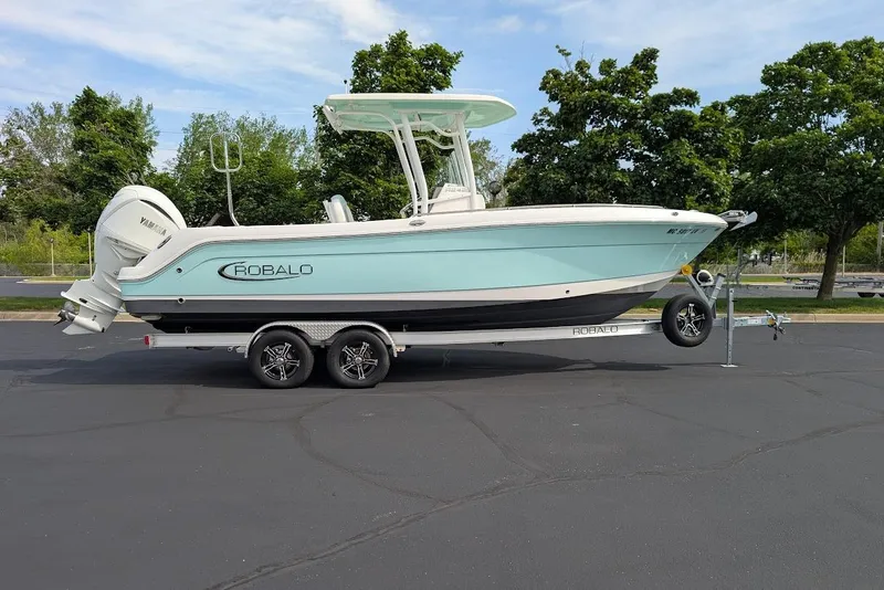 Slide: The Image of 2022 Robalo R242 Explorer boat on trailer, parked outdoors with trees in background. - 9