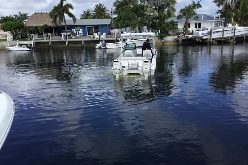 Slide: The Image of 2020 Twin Vee 240 DC GF boat navigating a calm waterfront near docks and palm trees. - 10