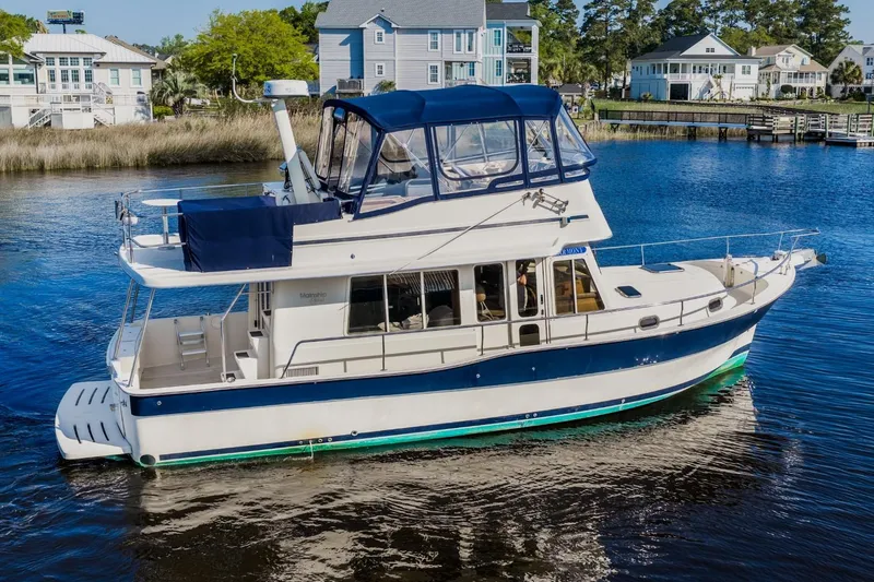 Slide: The Image of 2009 Mainship 40 Expedition yacht cruising on a serene waterway near waterfront homes. - 7