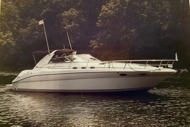 The Image of 1995 Sea Ray Sundancer 370 yacht cruising on a serene lake with forest backdrop. - 0