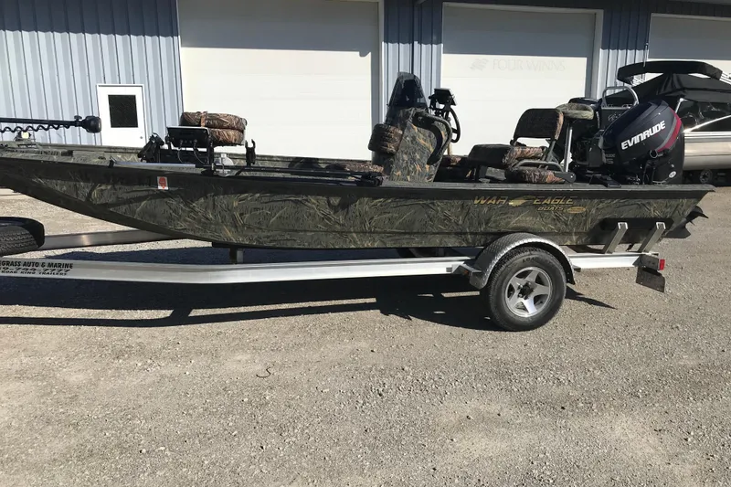 The Image of 2015 War Eagle 961 Blackhawk boat on trailer, camo design, parked outdoors. - 1