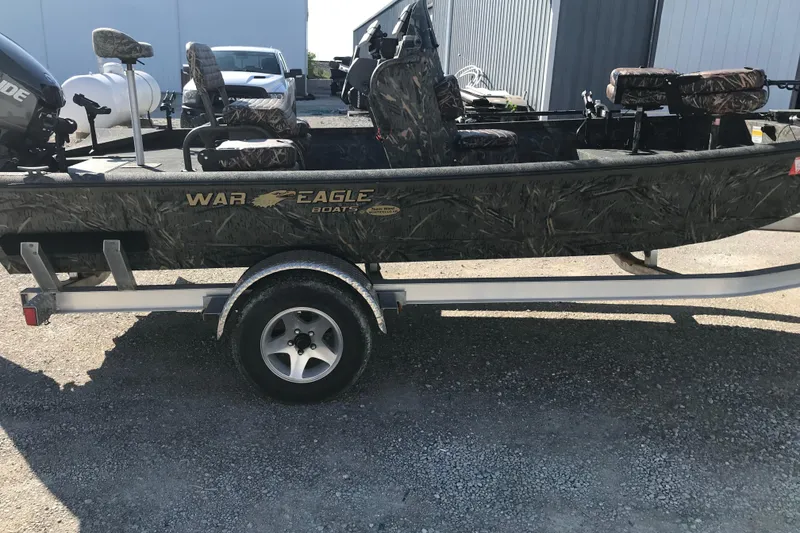 Slide: The Image of 2015 War Eagle 961 Blackhawk boat on trailer, camo design, parked outdoors. - 2