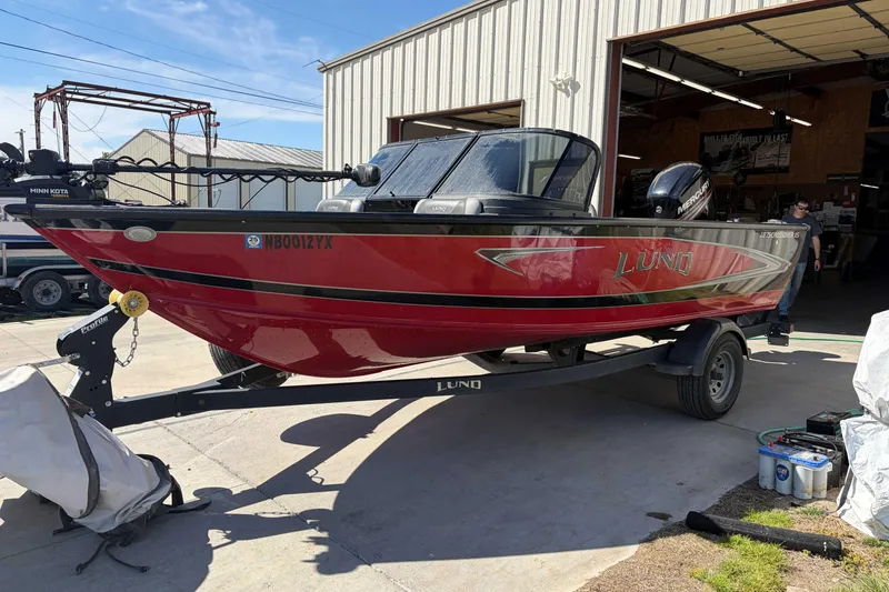 Slide: The Image of 2020 Lund 1875 Crossover XS boat in red, parked on a trailer outside a garage. - 2