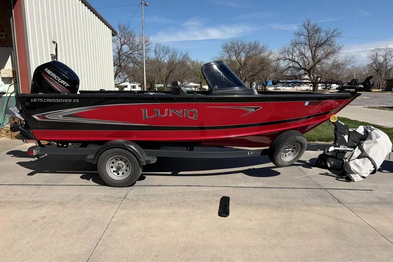 Slide: The Image of 2020 Lund 1875 Crossover XS boat in red, parked on a trailer outdoors. - 3