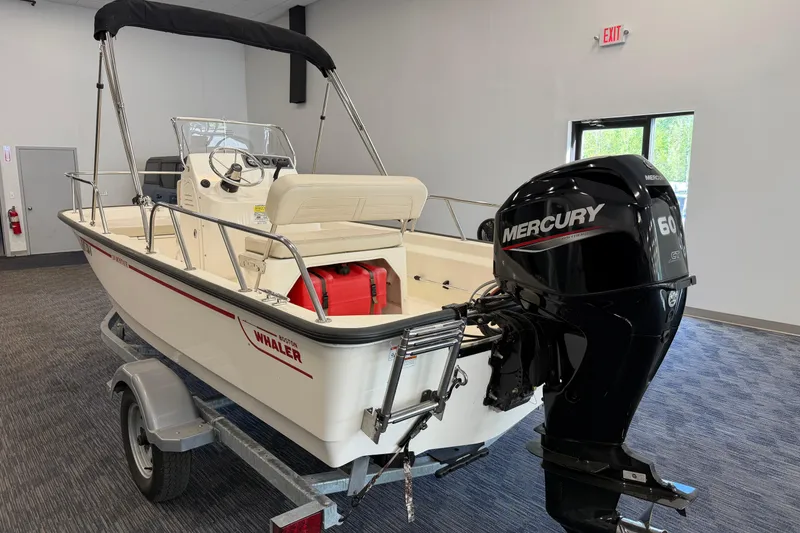 Slide: The Image of 2021 Boston Whaler 150 Montauk boat with Mercury 60 engine on trailer indoors. - 2