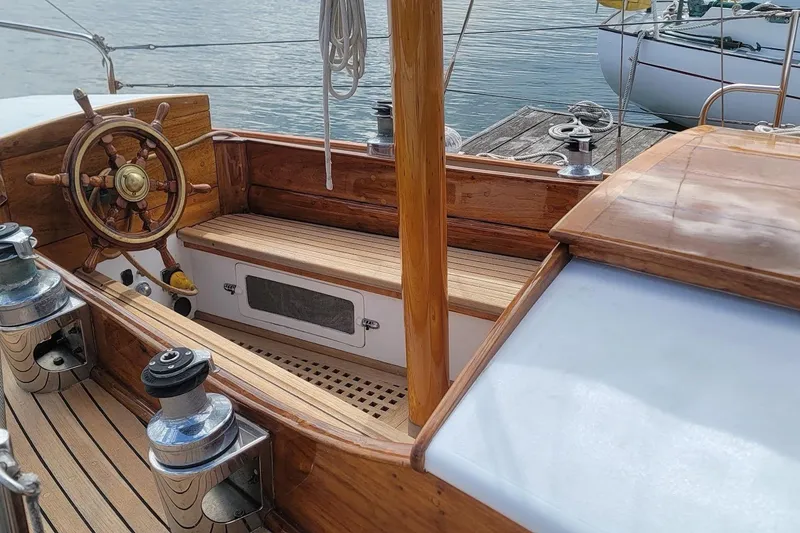 Slide: The Image of Wooden deck and helm of a 1936 Freeman 37 sailboat, docked by the water. - 2