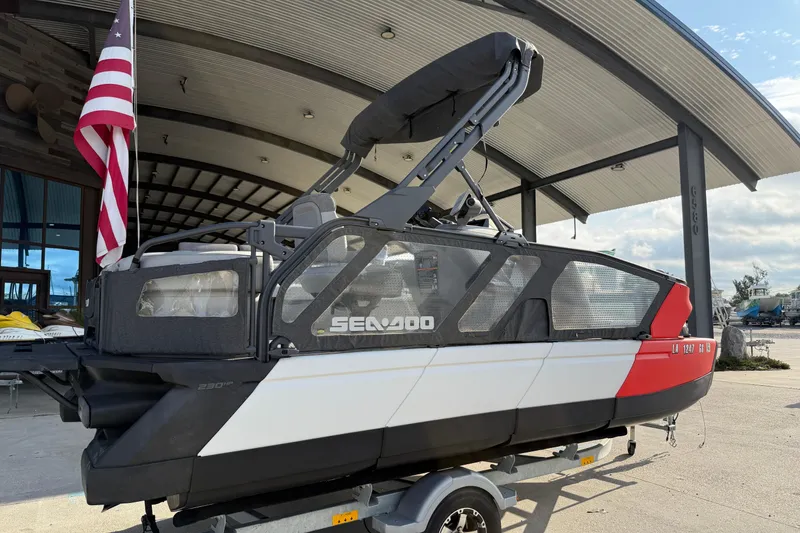 Slide: The Image of 2023 Sea-Doo Switch Sport 18 pontoon boat with American flag, docked under a canopy. - 2