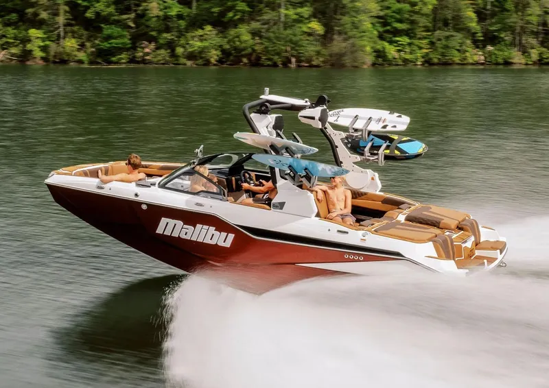 Slide: The Image of Manufacturer Provided Image: 2026 Malibu M230 boat cruising on a lake with passengers, surrounded by lush greenery. - 1