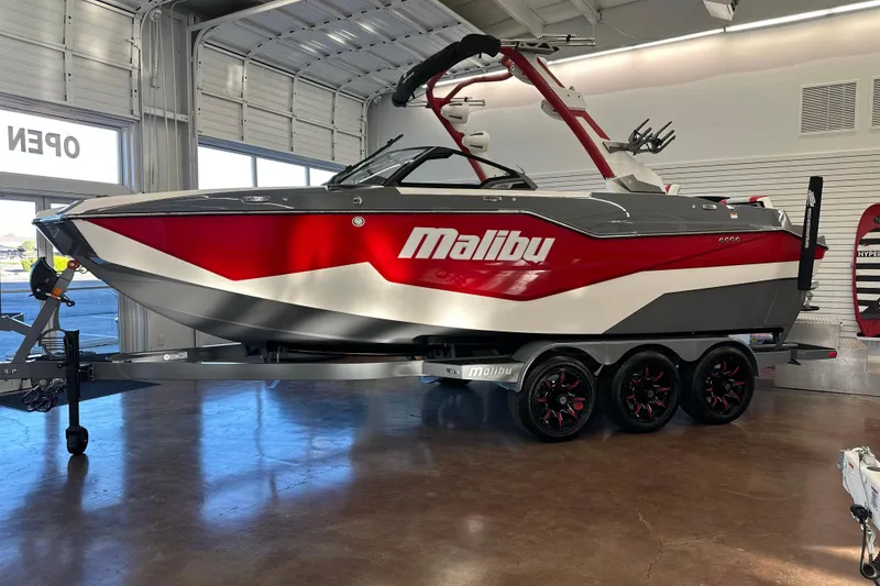 The Image of 2026 Malibu M230 boat in showroom, featuring sleek red and gray design on a trailer. - 8