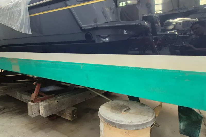Slide: The Image of 1990 Little Harbor Express boat hull in a workshop, featuring a green and white stripe. - 19