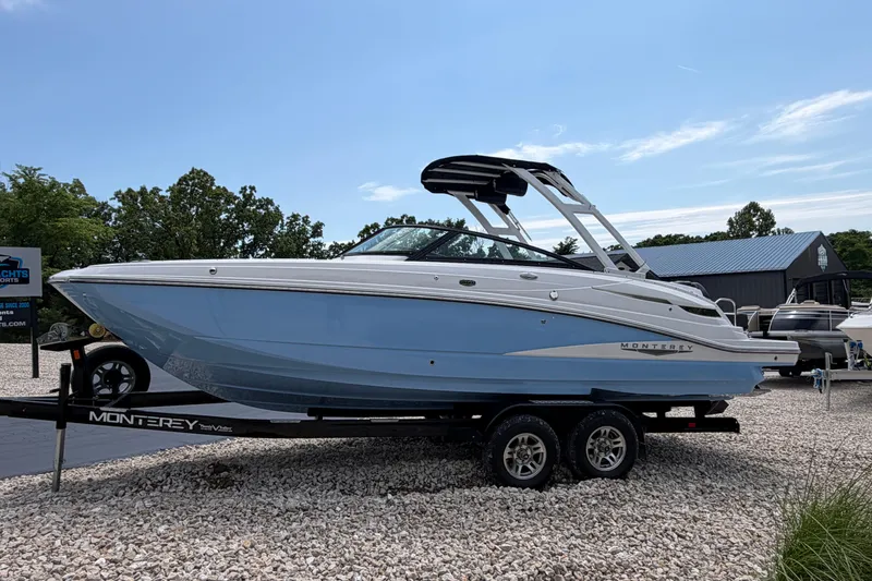 Slide: The Image of 2025 Monterey M6 boat on trailer, light blue hull, parked outdoors on gravel. - 2
