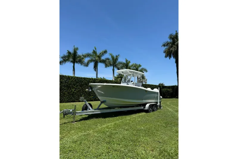 The Image of 2022 Blackfin 252 CC boat on trailer, parked on grass with palm trees in background. - 1