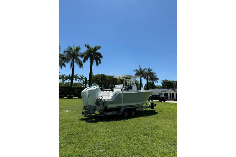 Slide: The Image of 2022 Blackfin 252 CC boat on trailer, parked on grassy area with palm trees. - 2