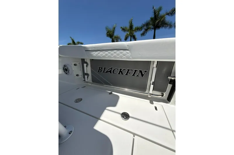 Slide: The Image of 2022 Blackfin 252 CC boat interior with logo, white seating, and palm trees in background. - 25