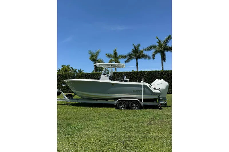 Slide: The Image of 2022 Blackfin 252 CC boat on trailer, parked on grass with palm trees in background. - 3