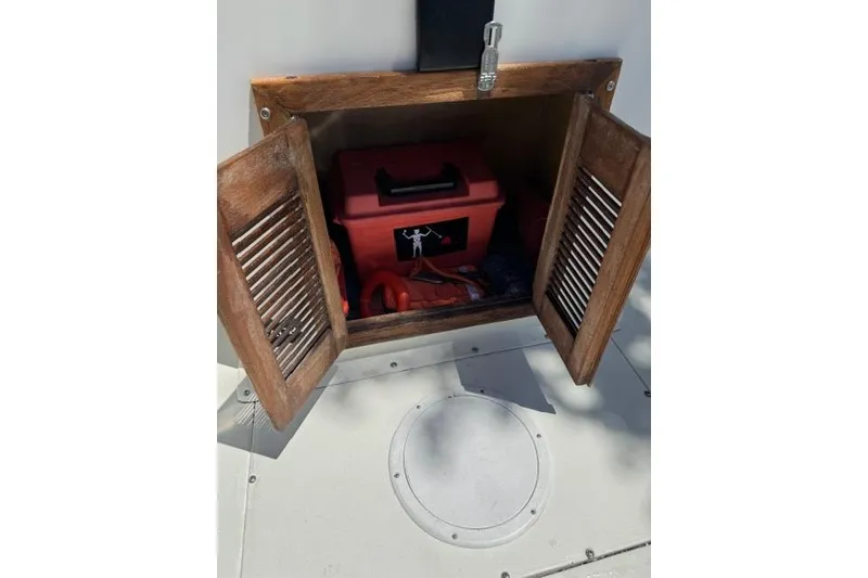Slide: The Image of Open wooden cabinet on 1987 Mako 232 Center Console boat, revealing red toolbox inside. - 21
