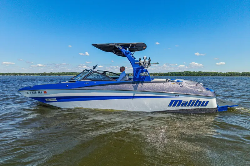 The Image of 2017 Malibu M235 boat cruising on a sunny lake with clear blue skies. - 0
