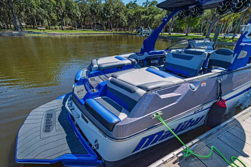 Slide: The Image of 2017 Malibu M235 boat docked on a calm lake, featuring sleek blue and gray seating. - 11
