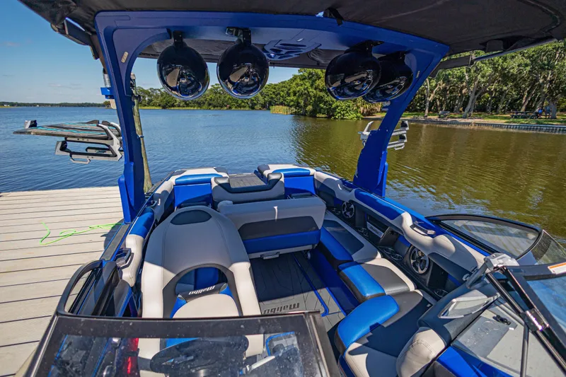 Slide: The Image of 2017 Malibu M235 boat interior with blue seating, docked by a serene lake. - 21