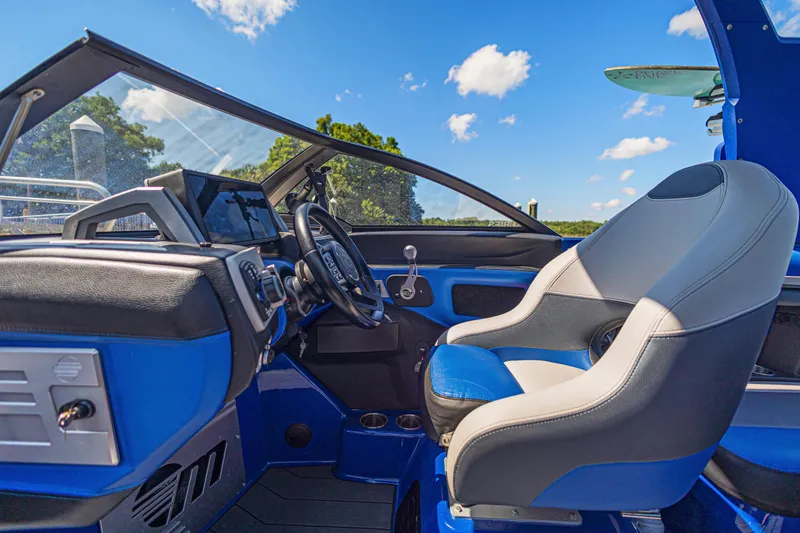 Slide: The Image of Interior of a 2017 Malibu M235 boat with blue and gray seating, steering wheel, and dashboard. - 23