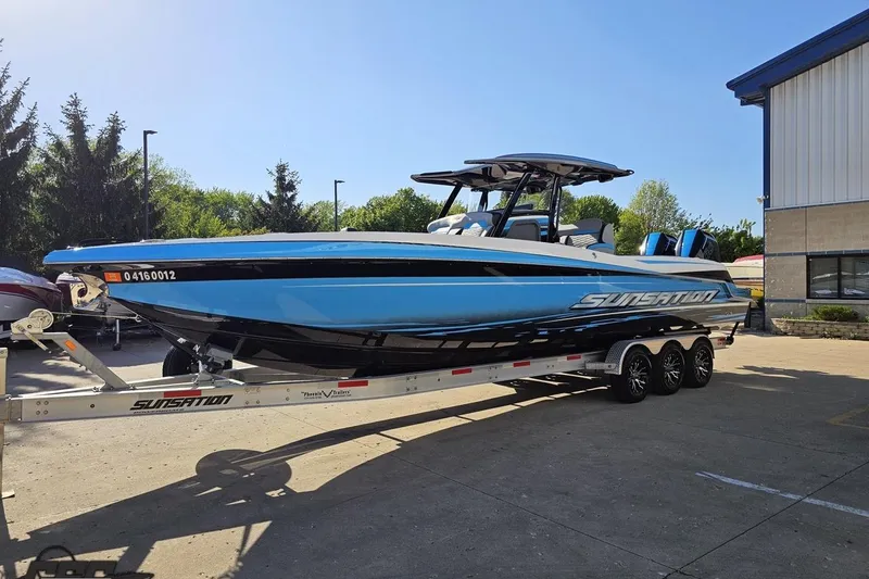 Slide: The Image of 2025 Sunsation 32 CCX boat on trailer, blue and black design, parked outdoors. - 22