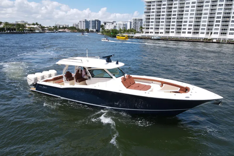 The Image of 2020 Scout 420 LXF luxury boat cruising on a sunny waterfront with cityscape backdrop. - 0