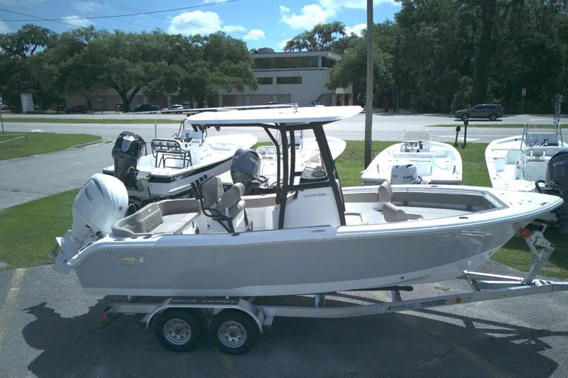 The Image of 2026 Sea Hunt Ultra 219 boat on trailer, parked outdoors, with trees and road in background. - 1