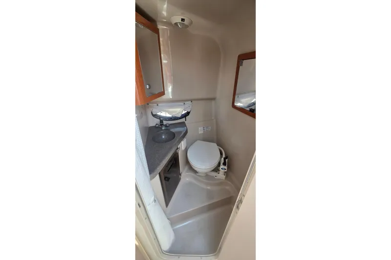 Slide: The Image of Compact bathroom in a 2001 Doral 250se boat, featuring a toilet, sink, and mirror. - 15