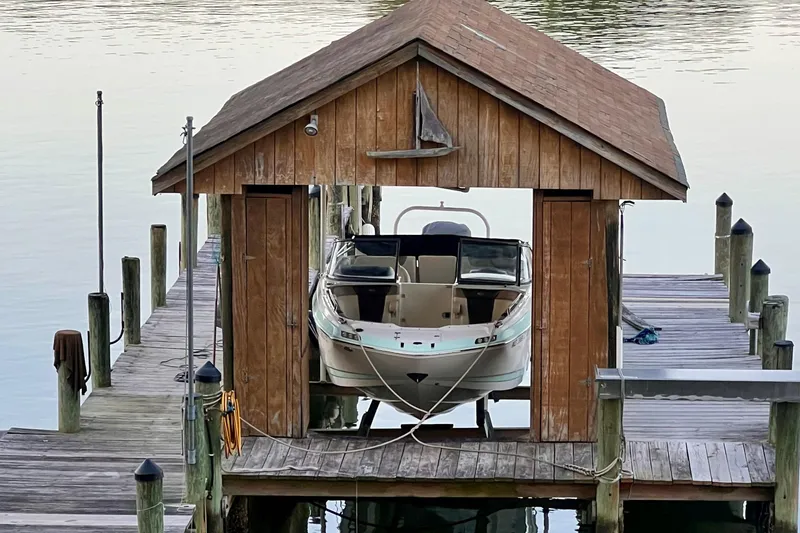 The Image of 2019 Chaparral 250 Suncoast boat docked in a wooden boathouse on calm water. - 2