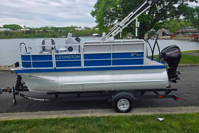 Slide: The Image of 2021 Lexington 315 pontoon boat on trailer by a lake, featuring a Mercury outboard motor. - 10