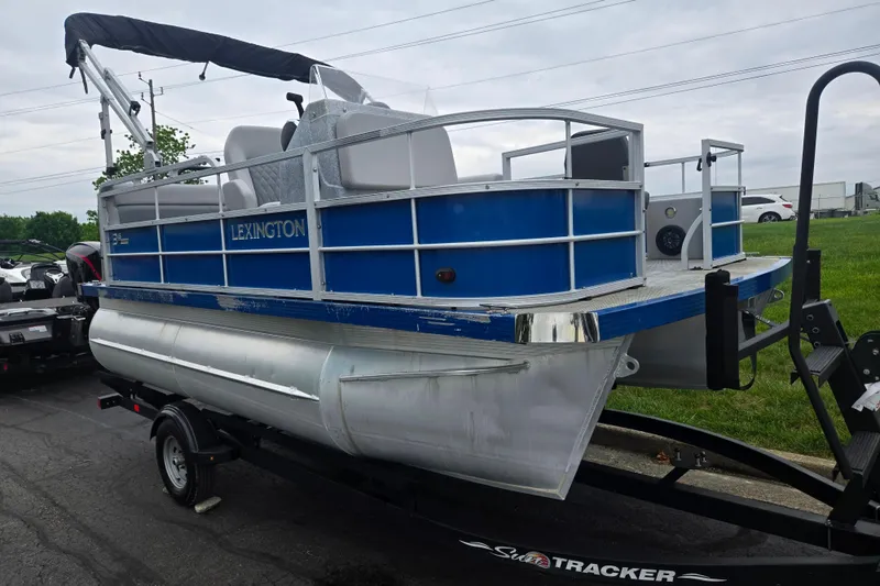 Slide: The Image of 2021 Lexington 315 pontoon boat on trailer, blue and silver design, parked outdoors. - 5