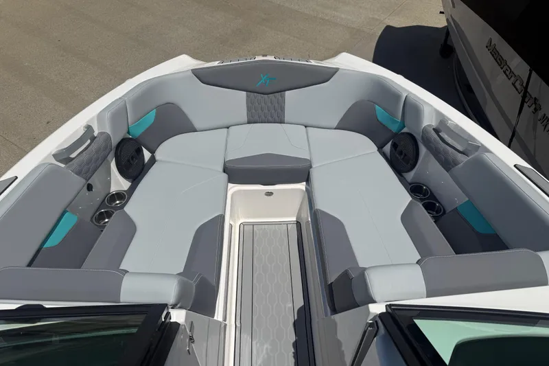 Slide: The Image of 2025 MasterCraft XT24 boat interior with gray and teal seating, cup holders, and speakers. - 2
