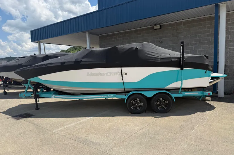 Slide: The Image of 2025 MasterCraft XT24 boat with cover on trailer, parked outdoors. - 27
