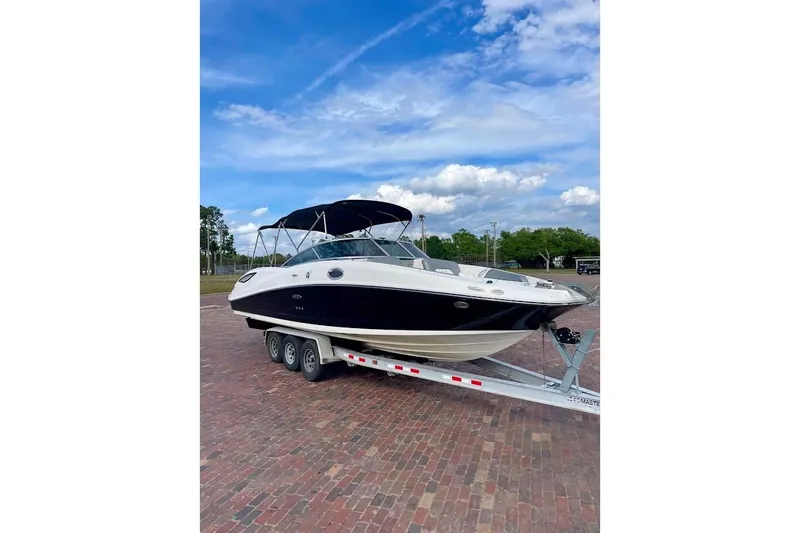 The Image of 2010 Sea Ray 300 Sundeck boat on trailer, parked on brick pavement under blue sky. - 1