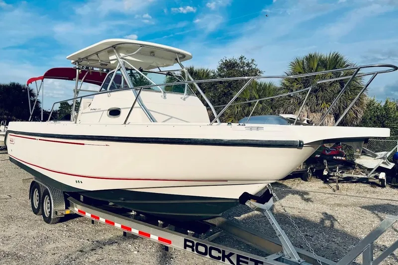 Slide: The Image of 2002 Boston Whaler 290 Outrage boat on trailer, parked outdoors under blue sky. - 6