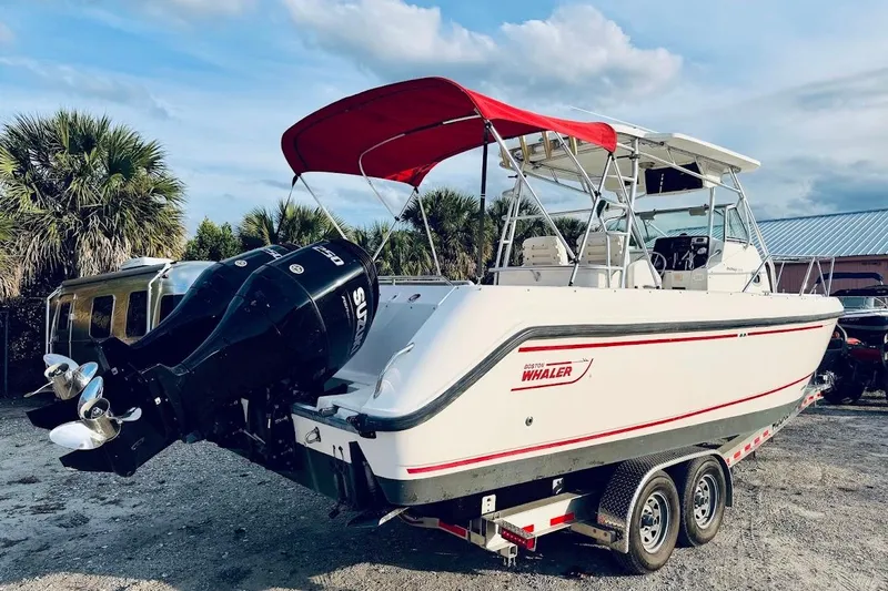 Slide: The Image of 2002 Boston Whaler 290 Outrage boat with red canopy on trailer, parked outdoors. - 7