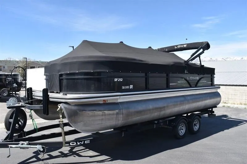 The Image of 2022 Lowe SF 212 Sport Fish pontoon boat on trailer, covered and parked outdoors. - 0