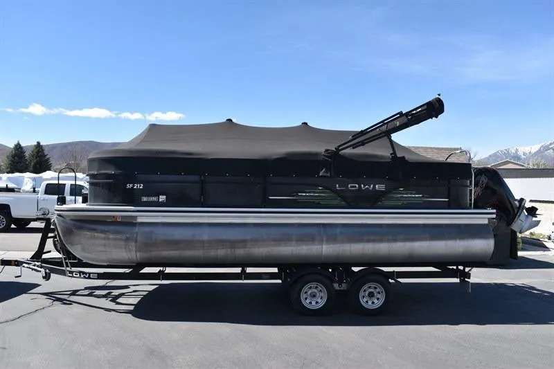 Slide: The Image of 2022 Lowe SF 212 Sport Fish pontoon boat on trailer, covered and parked outdoors. - 2