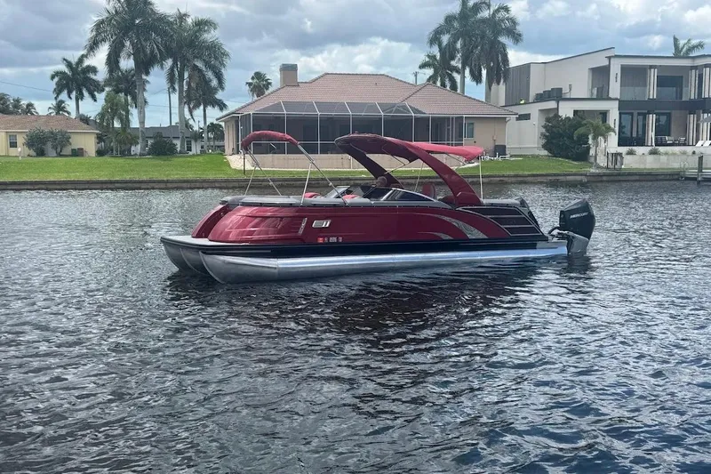 Slide: The Image of 2024 Bennington QX27 pontoon boat on a scenic waterfront with palm trees. - 2