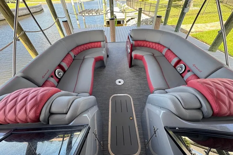 Slide: The Image of 2024 Bennington QX27 boat interior with luxurious red and gray seating, docked by the water. - 25