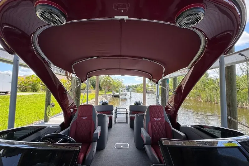 Slide: The Image of 2024 Bennington QX27 pontoon boat interior with luxurious seating and canopy on a scenic waterway. - 27
