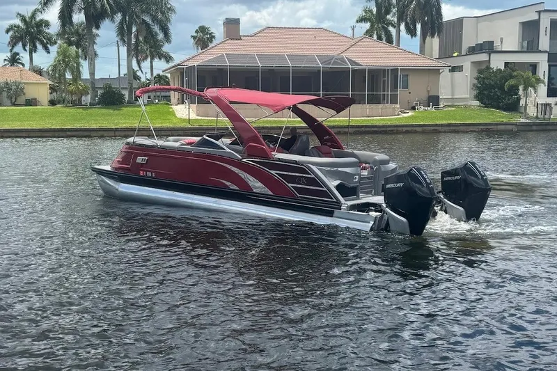Slide: The Image of 2024 Bennington QX27 pontoon boat cruising on a scenic waterway with modern homes. - 3