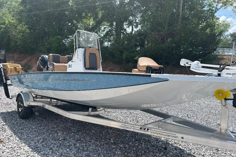 The Image of 2026 Xpress H20B Bay boat on trailer, parked on gravel, surrounded by trees. - 1