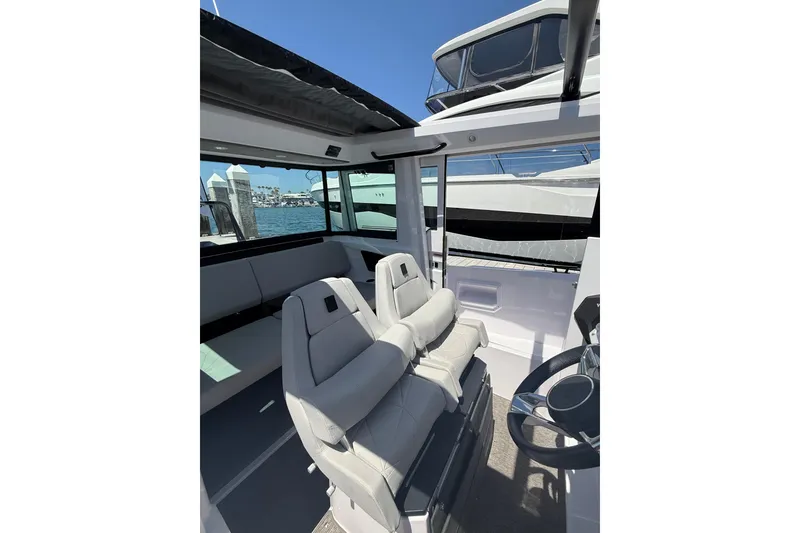 Slide: The Image of 2025 Axopar 29 XC Cross Cabin interior with modern seating and steering wheel, docked by the water. - 21