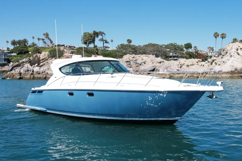 Slide: The Image of 2012 Tiara Yachts 4500 Sovran cruising near rocky shoreline under clear blue sky. - 3
