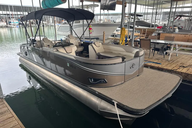 Slide: The Image of 2023 Avalon LSZ 2585 RL pontoon boat docked in marina, featuring spacious seating and canopy. - 2