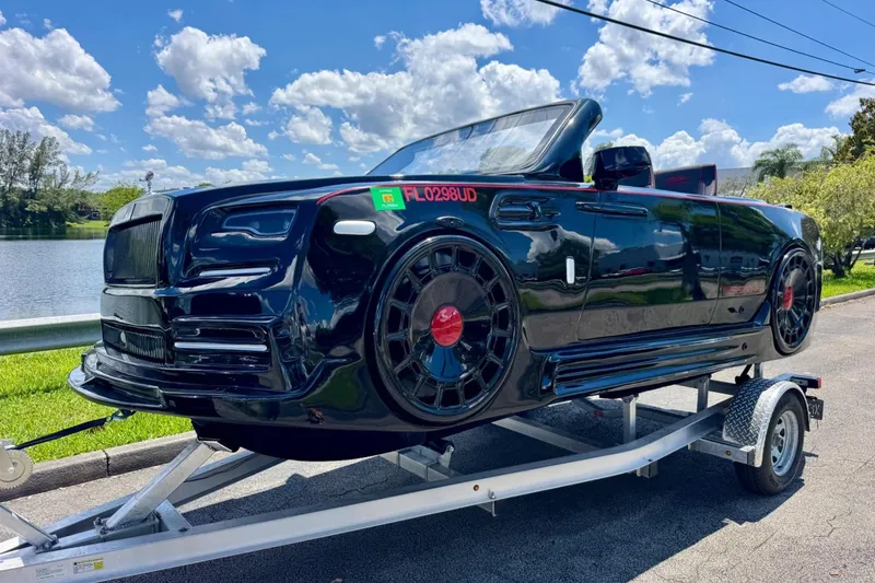 The Image of 2025 Watersports Car Series R on trailer, sleek black design, parked by a scenic lake. - 1